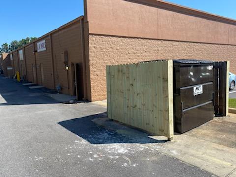 Dumpster stall with newly installed wood outside a shopping center with a dumpster in the stall | dumpster stall repair and installation | SprayTech, LLC