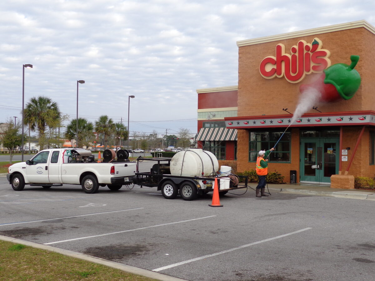 parking lot of Pensacola Chilis in which the building is being cleaned via a man holding a spraying that is attached to a commercial truck and tank | SprayTech, LLC